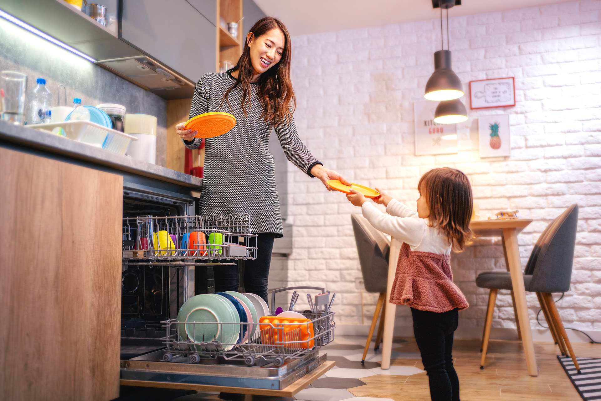 Happy mother and daughter loading a dishwasher